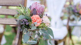 Hochzeits Gesteck aus Blumen im Glas an Stuhl befestigt