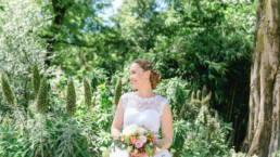 Braut in weiss mit schönen Brautstrauss gemacht von BLUAMAZAINA steht in Botanischem Garten